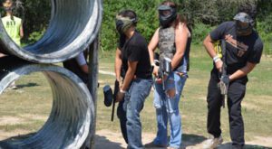 two girls and a man hiding during paintball game
